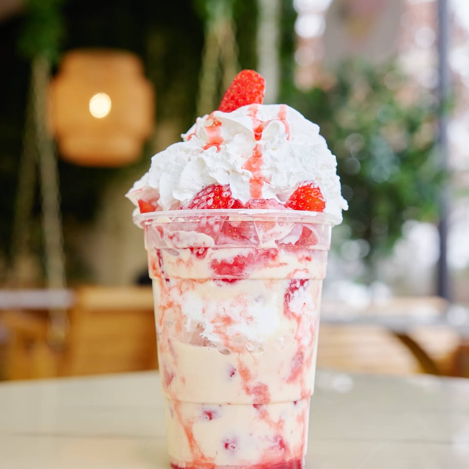 Strawberry-and-cream dessert drink topped with whipped cream and fresh strawberries, displayed on a café table.