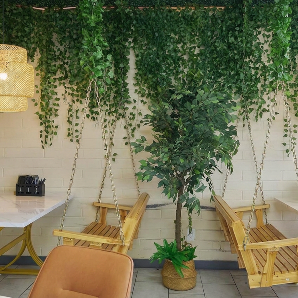 Bright restaurant interior with hanging wooden swing chairs, marble tables, woven pendant lights, and lush greenery against a white brick wall.