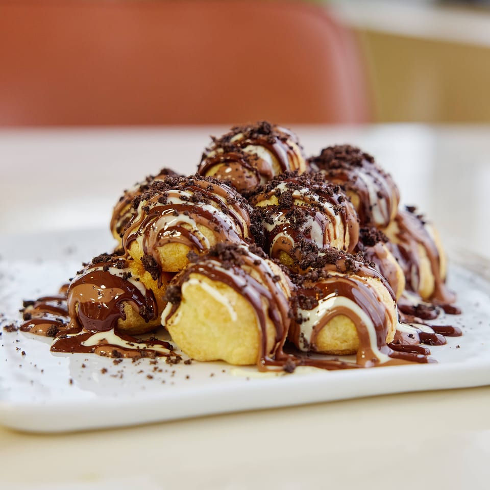 Golden cream-filled pastries drizzled with chocolate and white icing, topped with cookie crumbs on a white plate.