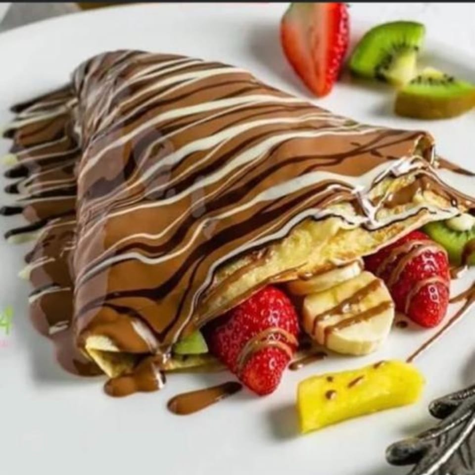 Crepe drizzled with chocolate and white icing, filled with fruit and served with strawberries, bananas, kiwi, and pineapple.