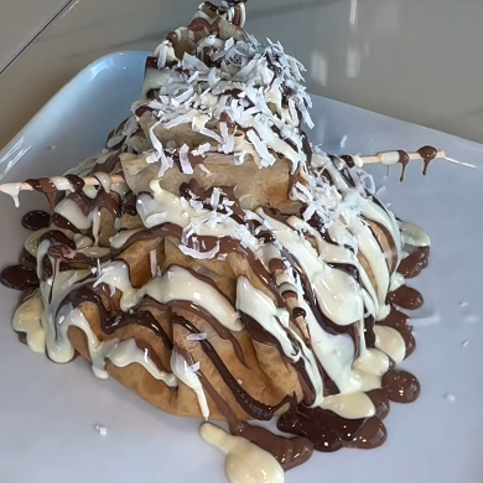 Stacked dessert drizzled with chocolate and vanilla sauces, topped with shredded coconut and served on a white plate.