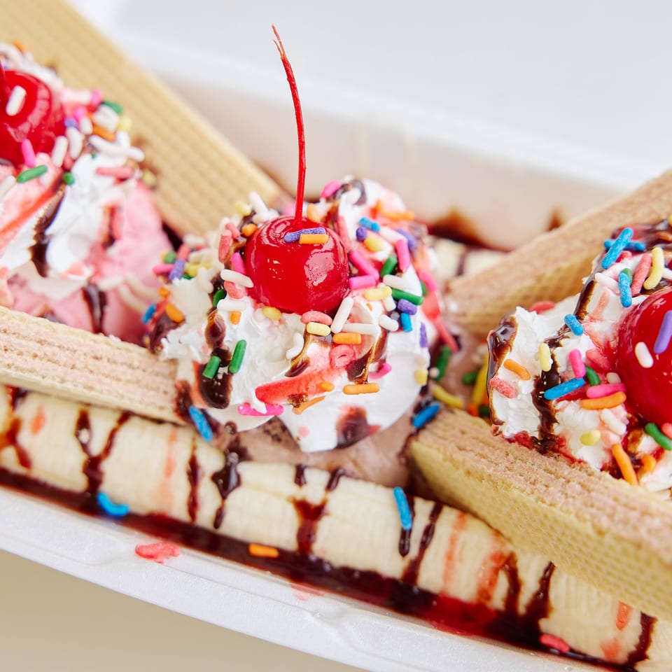 Banana split topped with vanilla ice cream, cherries, colorful sprinkles, chocolate syrup, and wafer cookies.