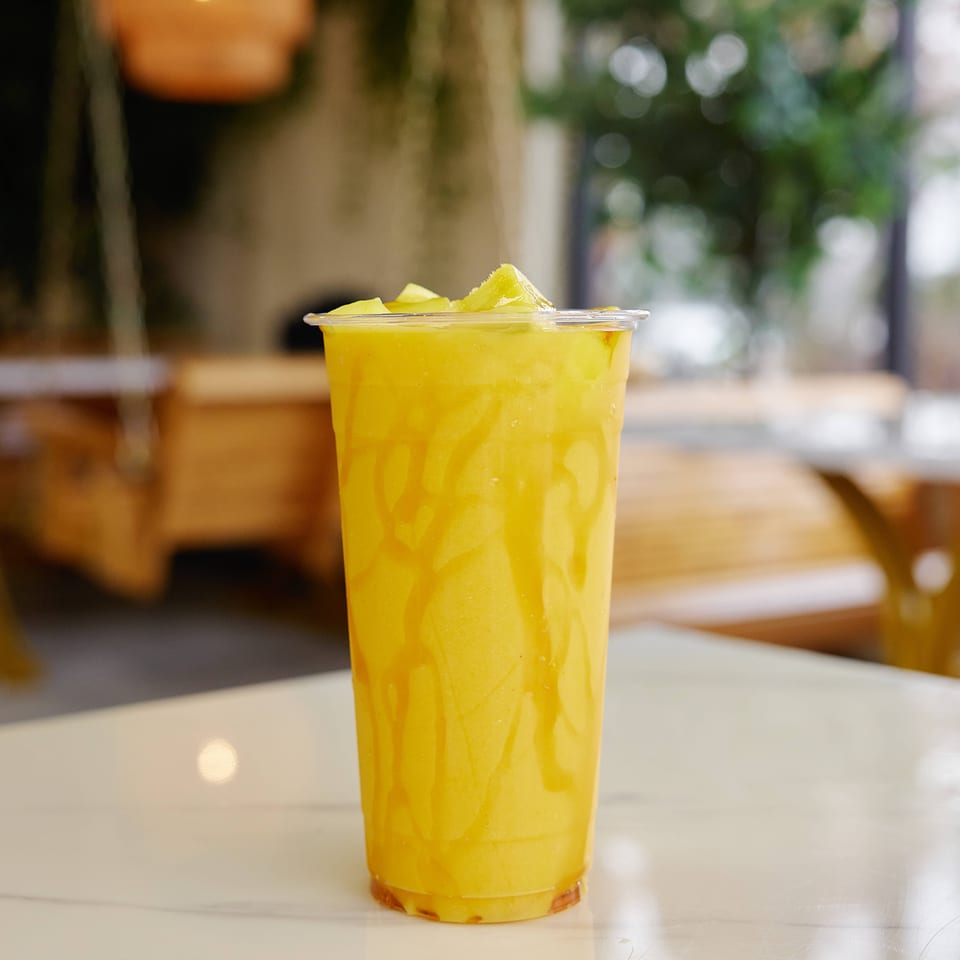 Tall yellow citrus drink topped with lime wedges, served in a clear cup on a restaurant table.